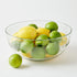 Clear glass bowl filled with lemons and limes on a white background