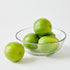 Green limes in a clear glass bowl on a white background