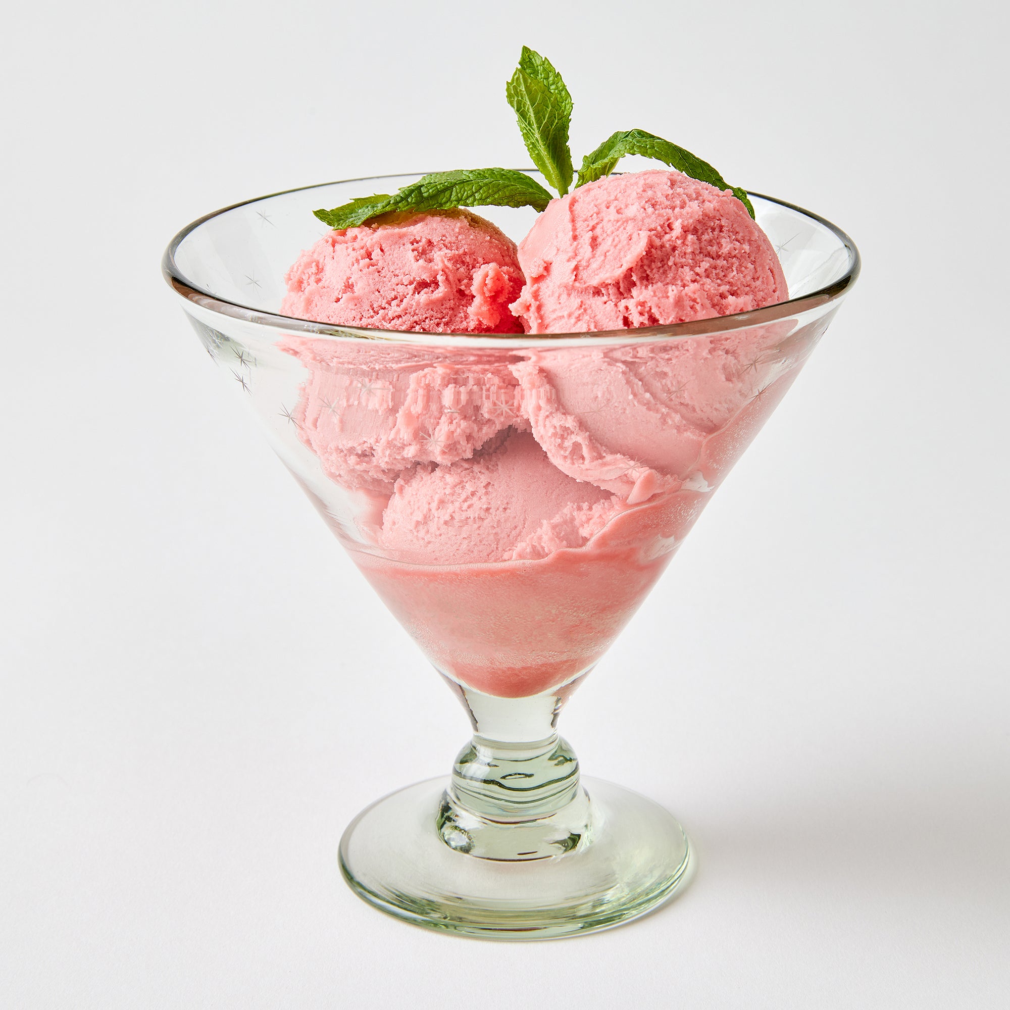 Strawberry ice cream in a footed dish glass  etched with stars with mint leaves on a white background