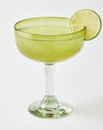 Cocktail in a yellow margarita glass etched with stars with a lime wheel on a white background