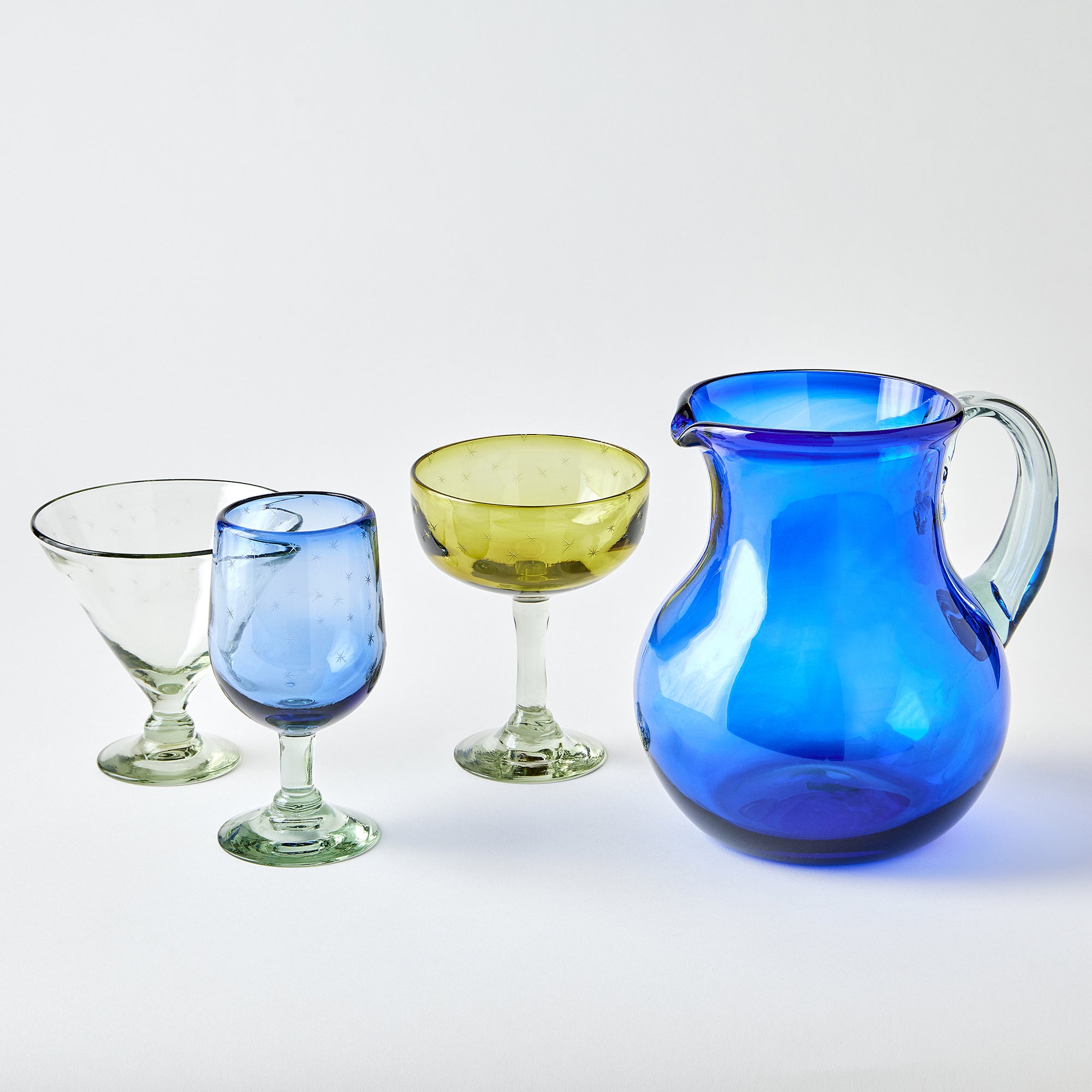 Set of colorful glassware including a blue pitcher and various glasses on a white background
