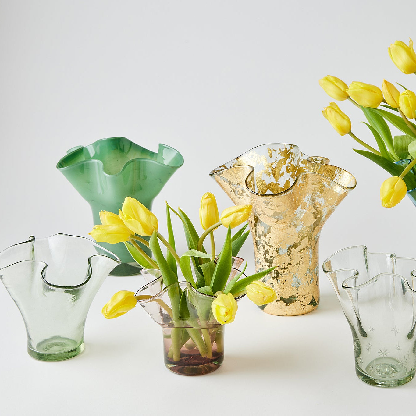 Collection of glass vases with yellow tulips on a white background