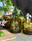 Brown glasses with ice and lime wedges on a wooden table with flowers in the background.